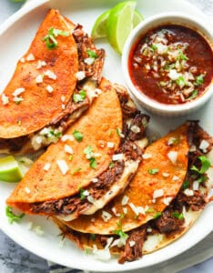 Beef birria tacos with extra birria sauce and a lime wedge