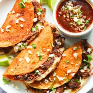 Beef birria tacos with extra birria sauce and a lime wedge