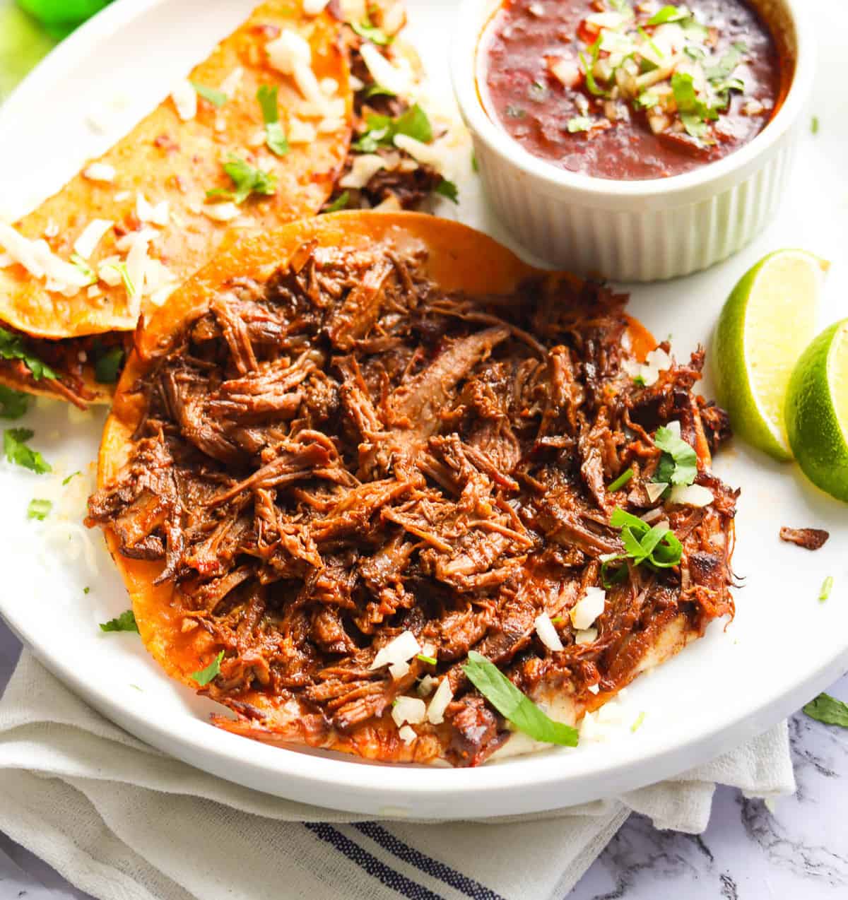 Mouthwatering beef birria tacos with refried beans and lime wedges