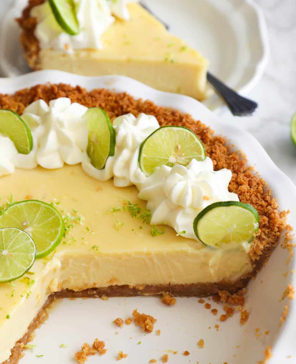 Sliced Key Lime Pie with a slice on a white plate in the background
