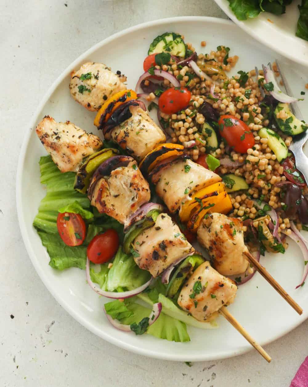 Two chicken kabobs on a plate with couscous