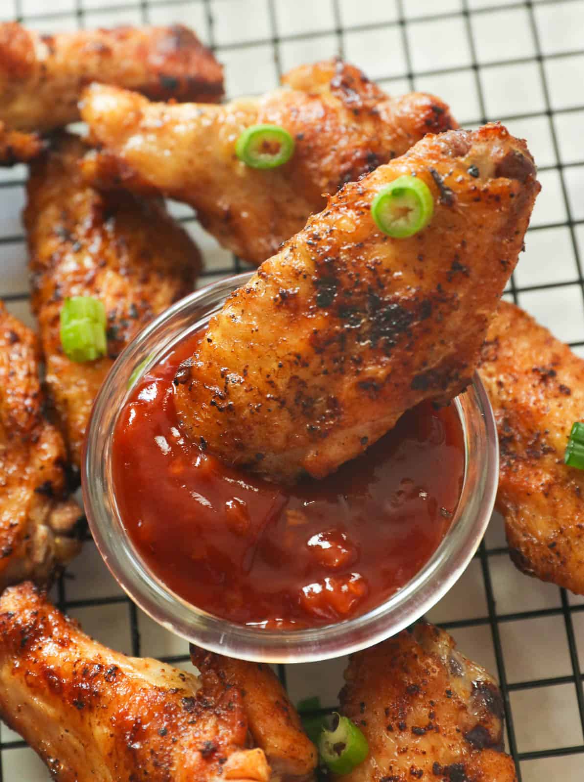 Dipping crispy grilled chicken wings in red sauce