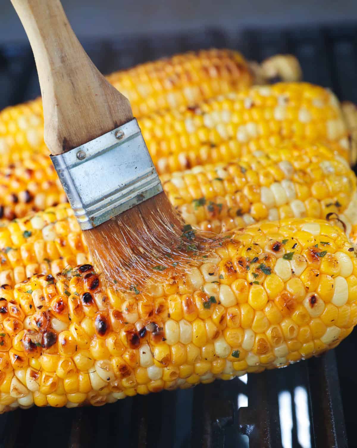 Brushing grilled corn on the cob with garlic butter