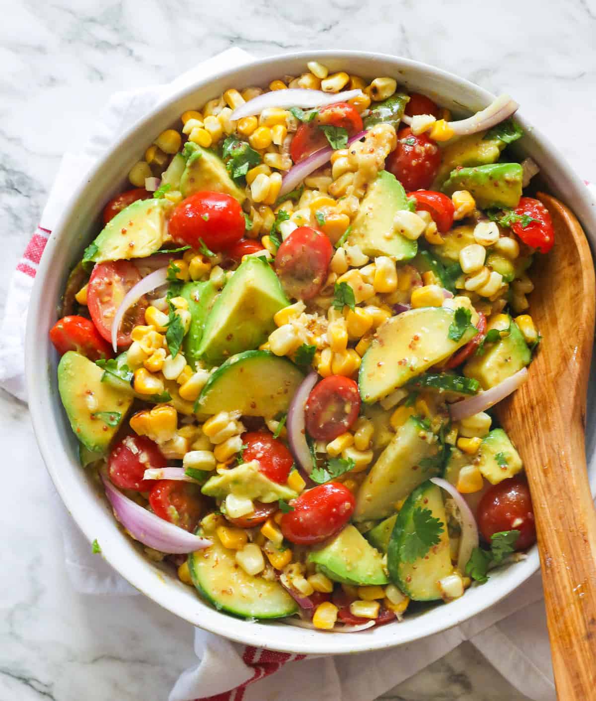 A bowl of avocado corn salad with a wooden spoon