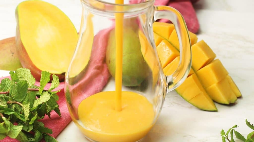 Pouring mango juice into a pictcher with mango in the background