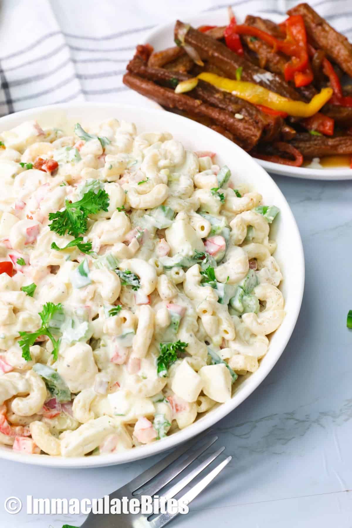 A bowl of macaroni salad with an entree in the background