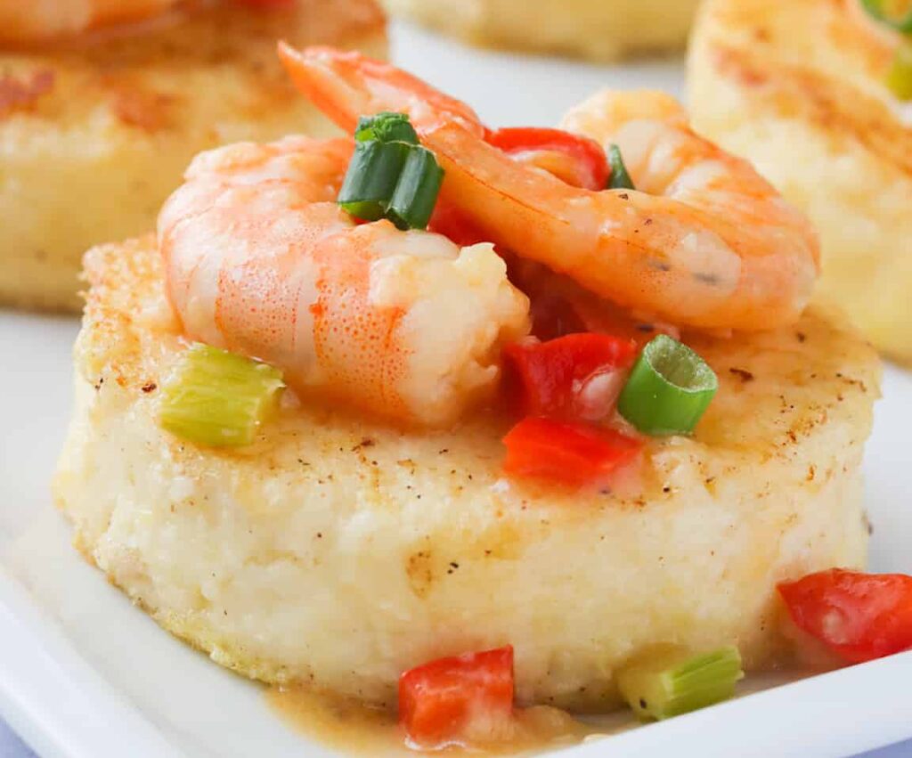 A platter of grit cakes topped with sauce and shrimp
