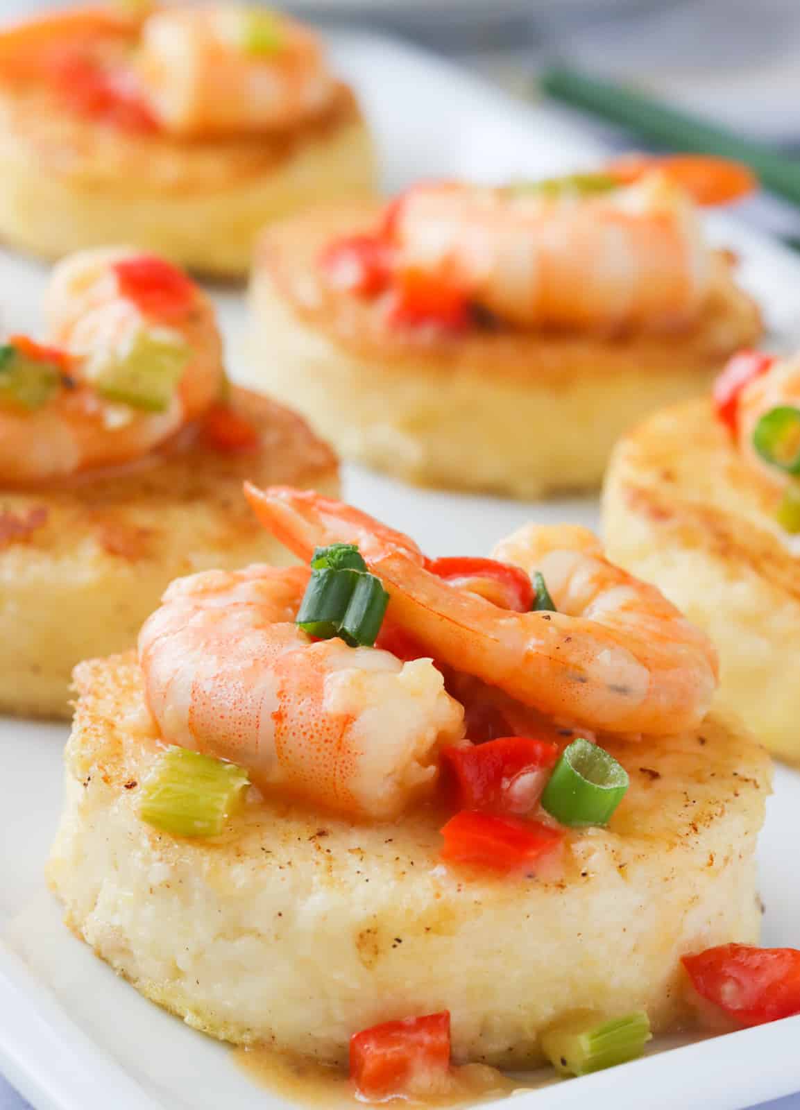 A platter of grit cakes topped with sauce and shrimp