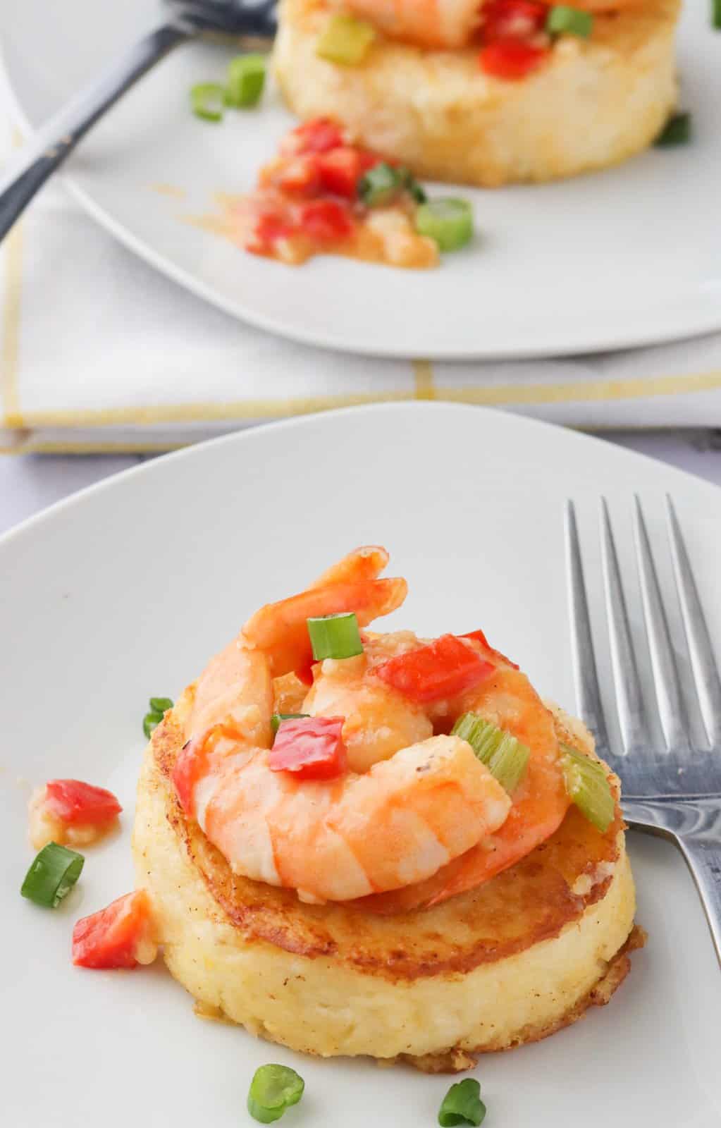 Grit cakes topped with shrimp on a white plate with a fork