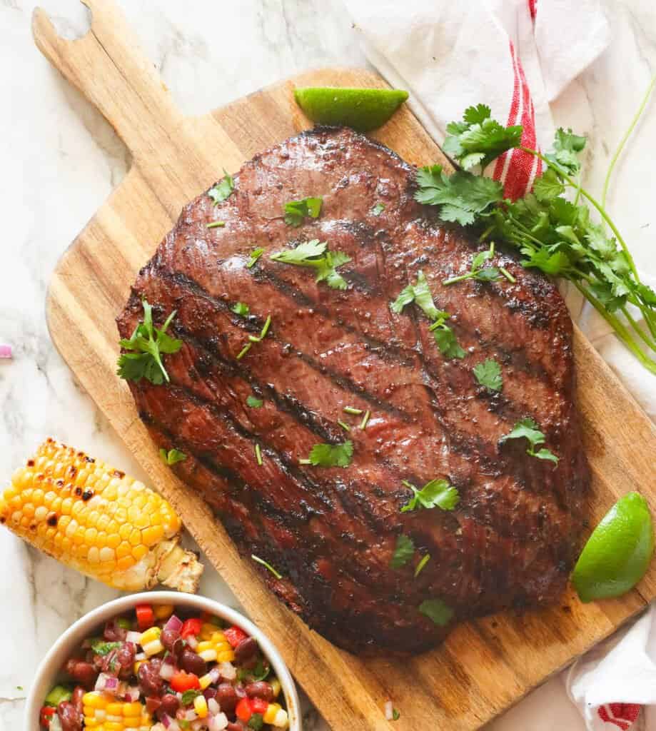 Grilled flank steak on a wooden cutting board with lime and herbs