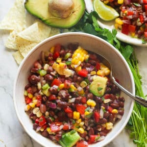 A bowl of black bean and corn salad with an avacodo and tortilla chips in the background