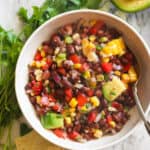 Black bean and corn salad in a white bowl with cilantro in the background