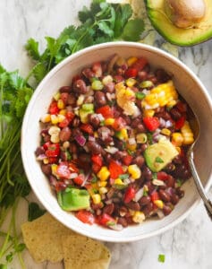 Black bean and corn salad in a white bowl with cilantro in the background