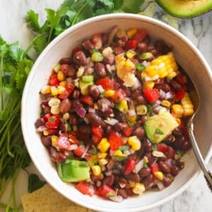 Black bean and corn salad in a white bowl with cilantro in the background
