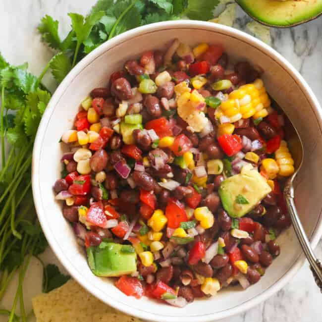 Black bean and corn salad in a white bowl with cilantro in the background