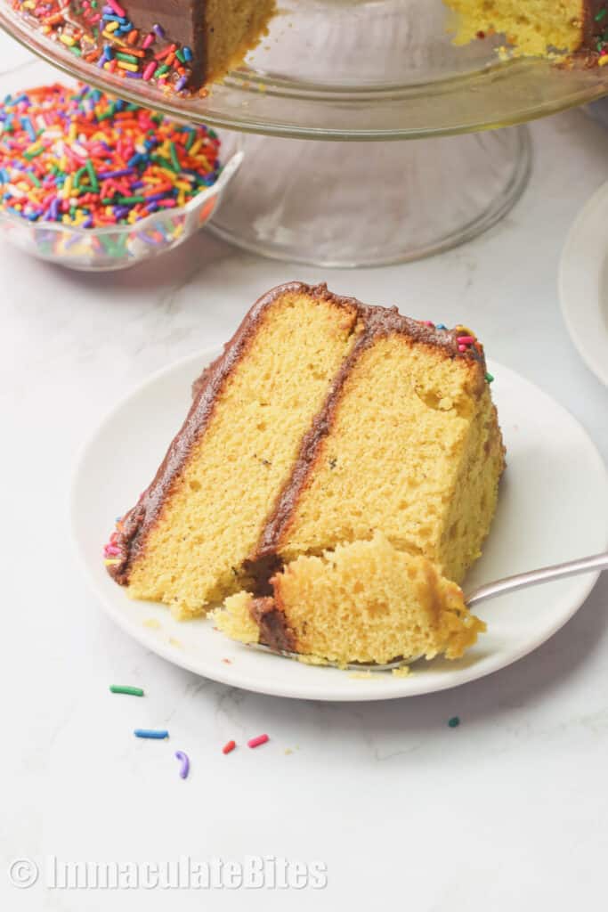 A slice of yellow cake on a white plate with a fork