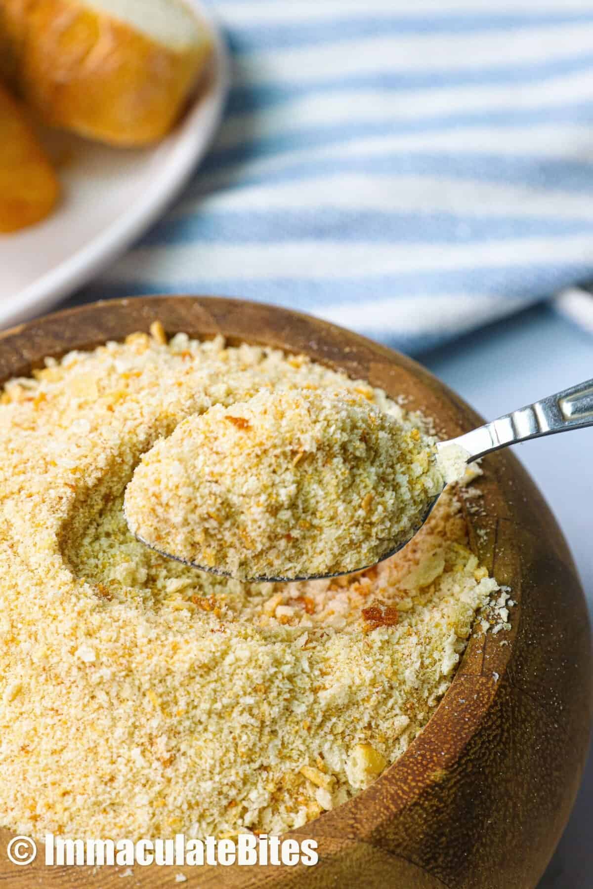 A wooden bowl of homemade breadcrumbs with a spoon