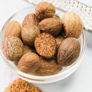 Whole nutmeg in a bowl with a microplane and some grated nutmeg on the side