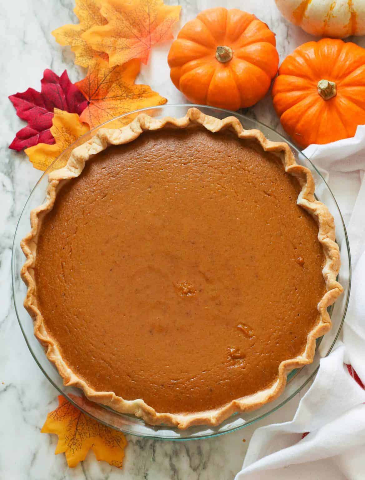 A whole pumpkin pie with decorative pumpkins in the background
