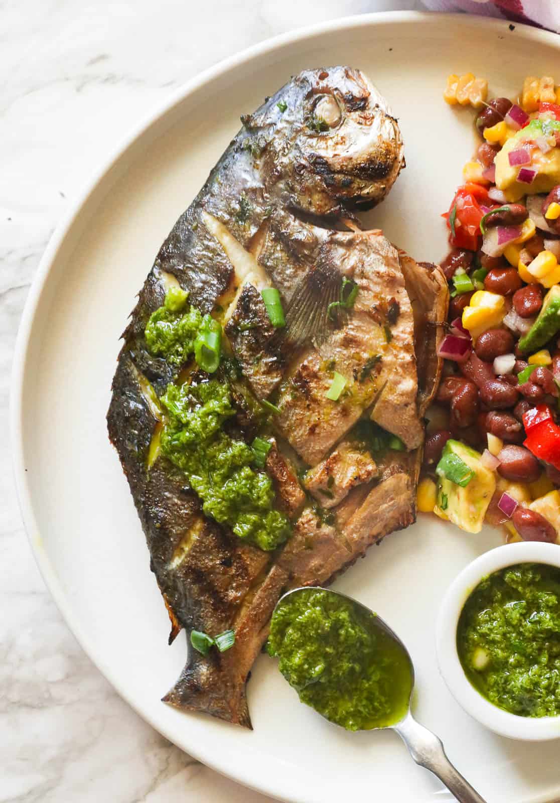 Whole grilled pompano on a white plate with black bean and corn salsa