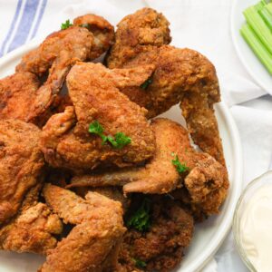 A plate piled high with fried chicken wings and hot sauce and remoulade on the side