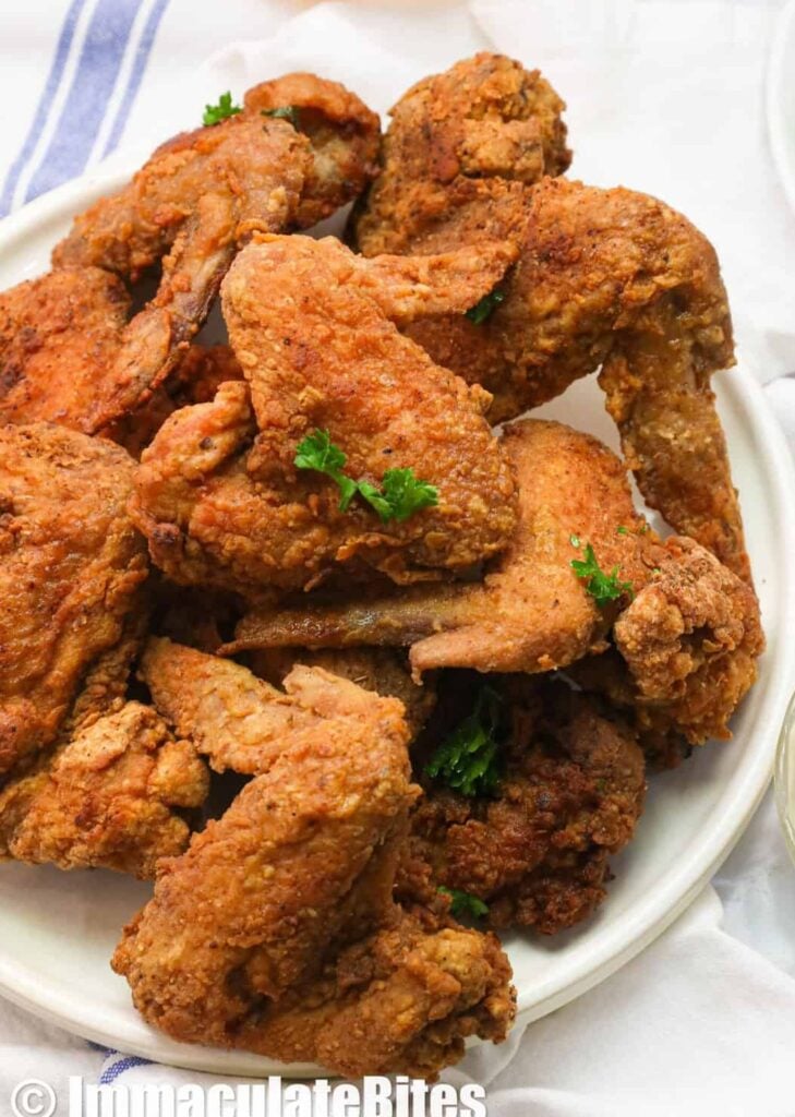 A plate piled high with fried chicken wings and hot sauce and remoulade on the side
