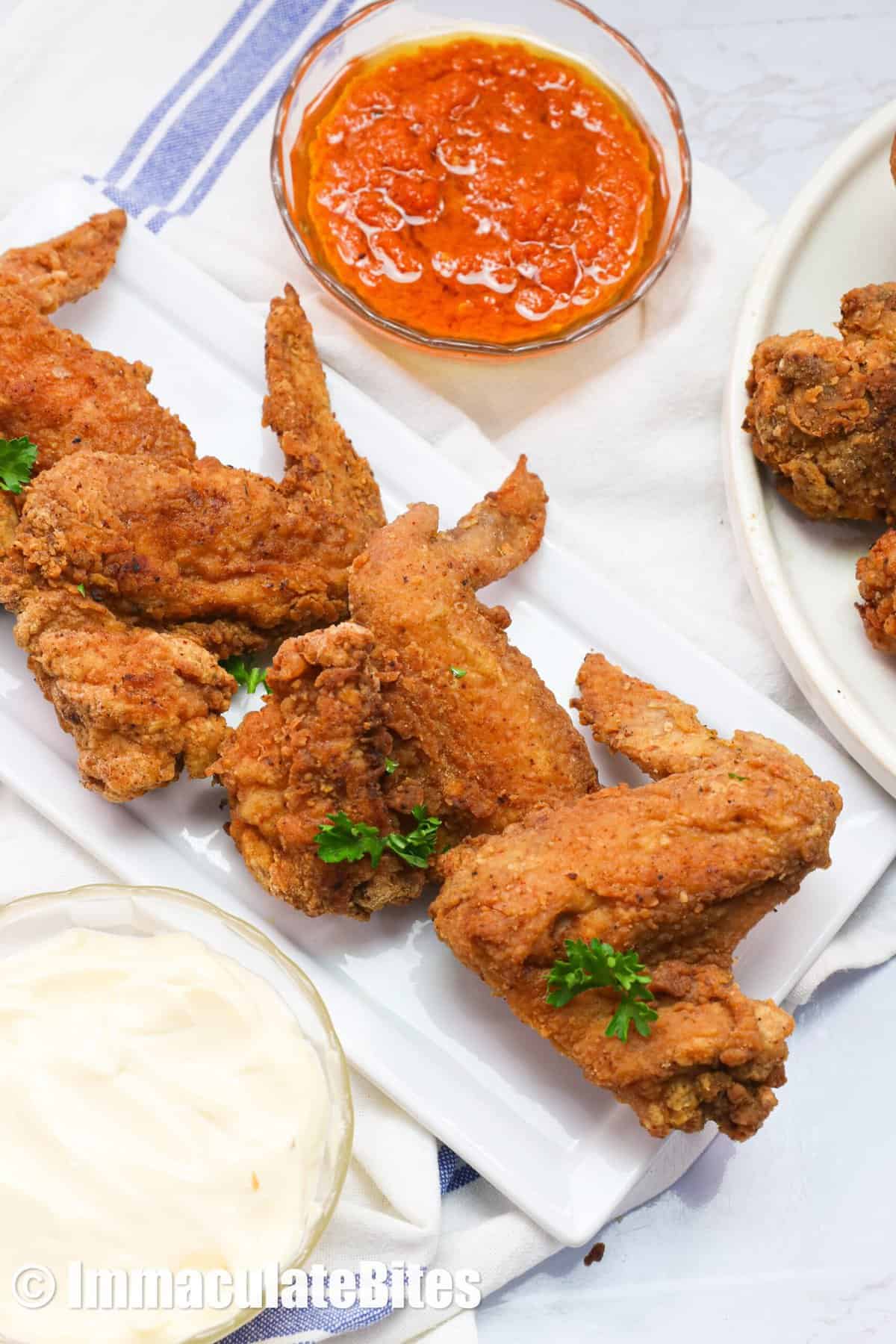 Four fried chicken wings on a white rectangular plate, served with hot sauce and remoulade
