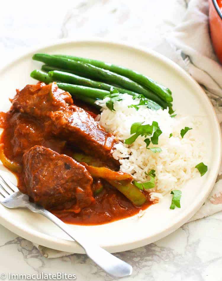 Swiss steak with white rice and green beans on a white plate
