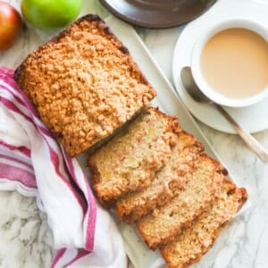 Freshly baked apple bread with a cup of coffee and fresh apples next to it