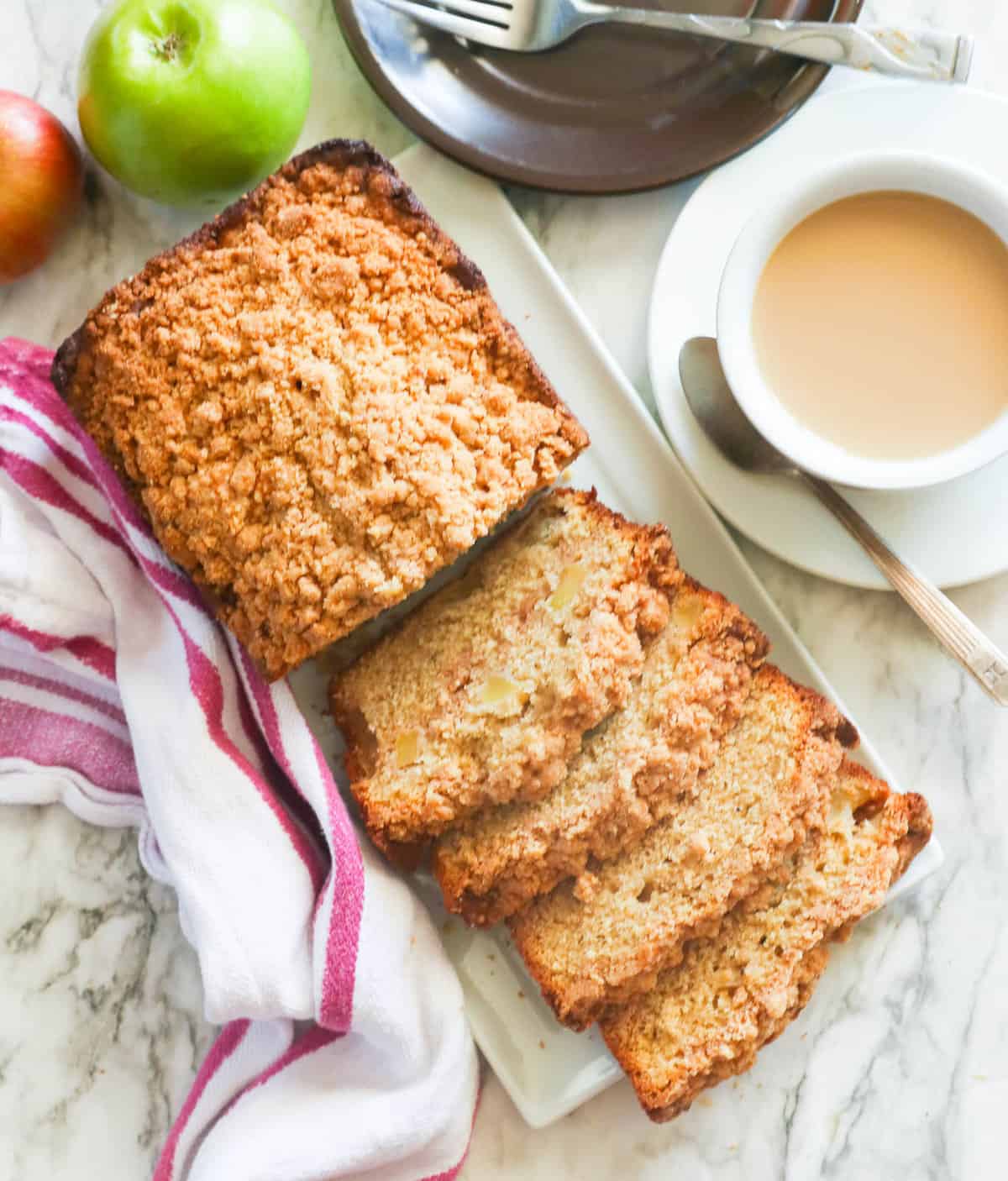Freshly baked apple bread with a cup of coffee and fresh apples next to it