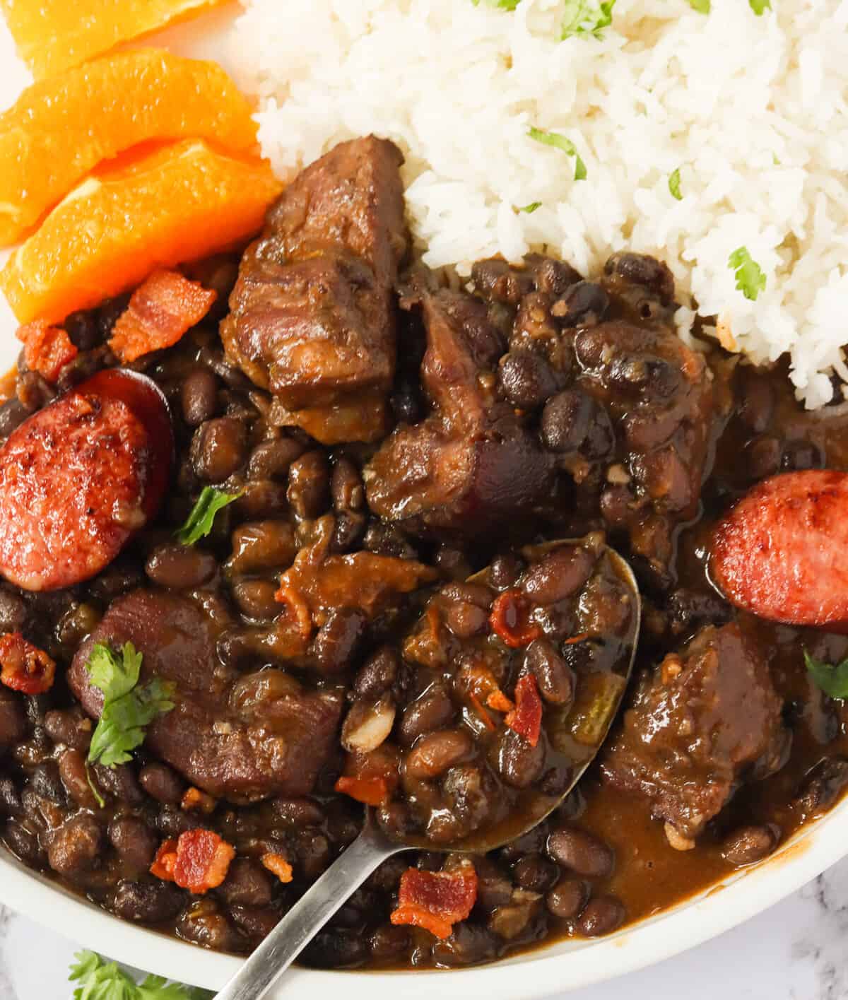 A bowl of hearty feijoada served with rice and orange slices