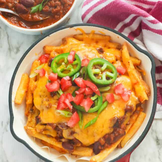 A skillet full of Texas chili cheese fries with more chili in the background