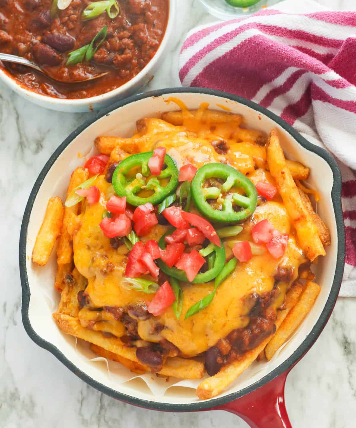 A skillet full of Texas chili cheese fries with more chili in the background