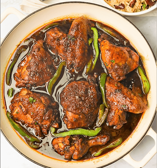 A pot of fresh brown stew chicken with Caribbean rice and beans on the side