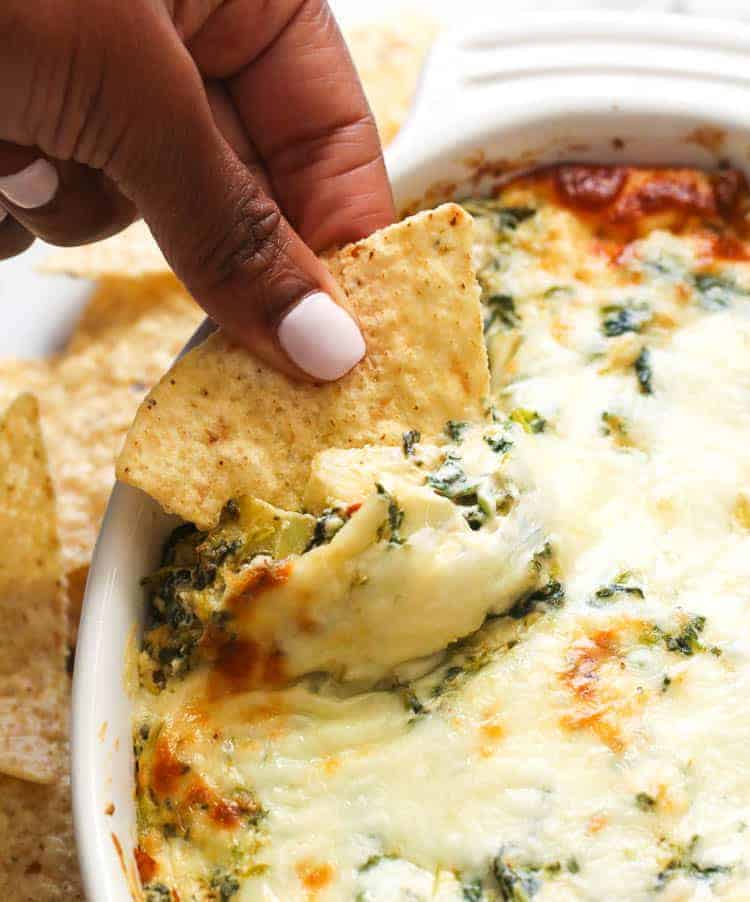 Taking a scoop of Spinach Artichoke Dip with a corn chip