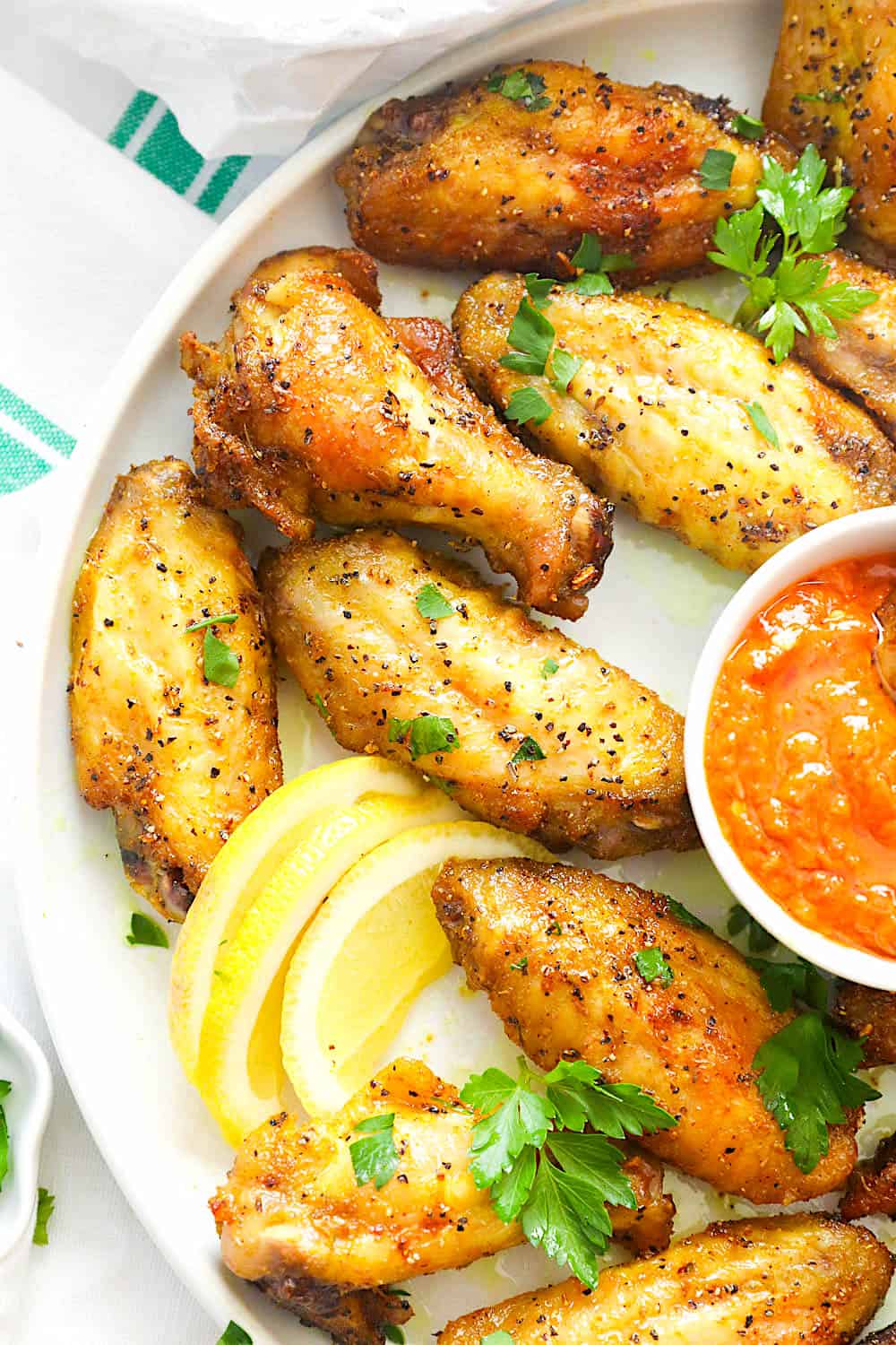 Lemon pepper chicken wings on a platter with hot sauce and lemon slices