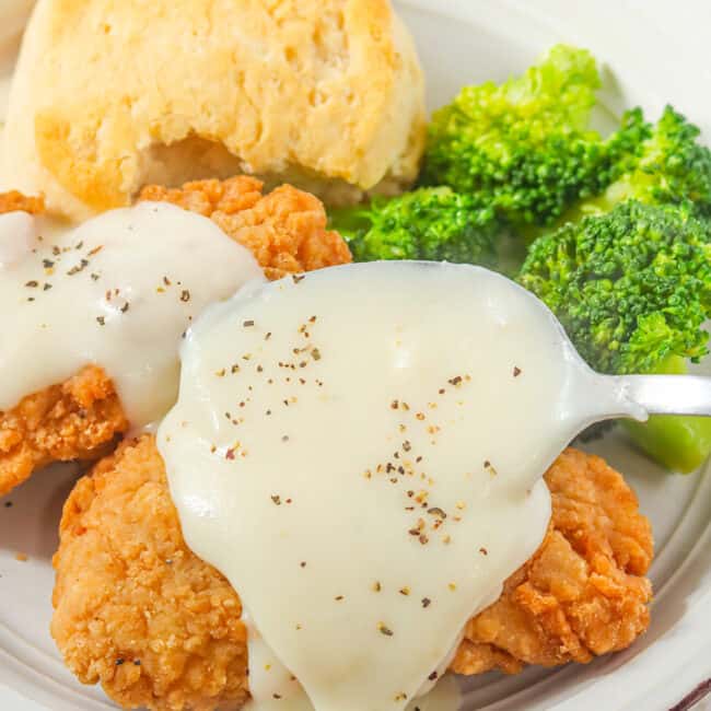 Slathering tasty white gravy over fried chicken and biscuits