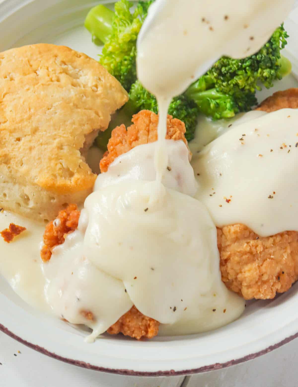 Drizzling rich white gravy over fried chicken and biscuits