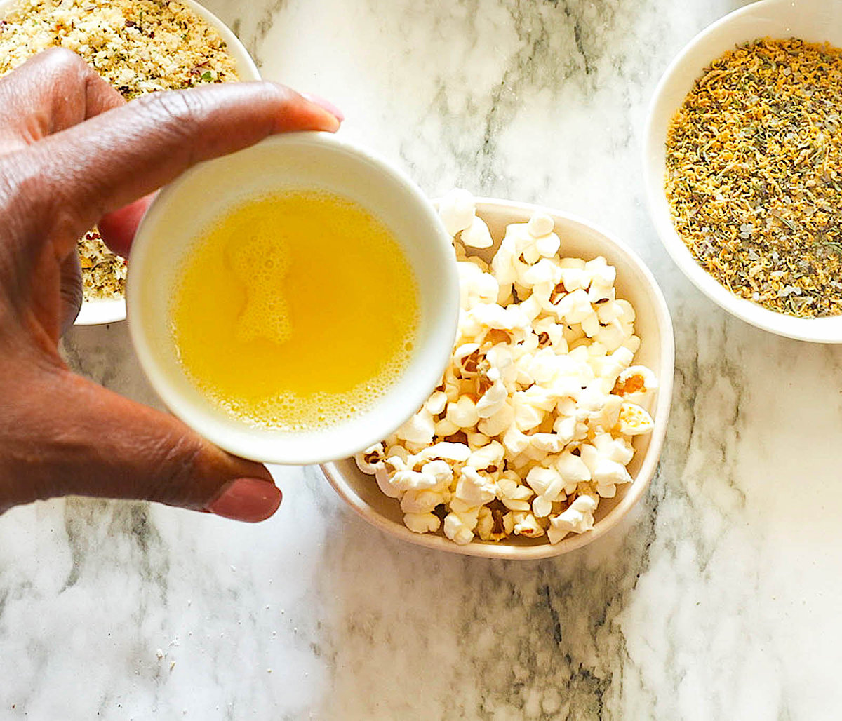 Pouring melted butter over seasoned popcorn