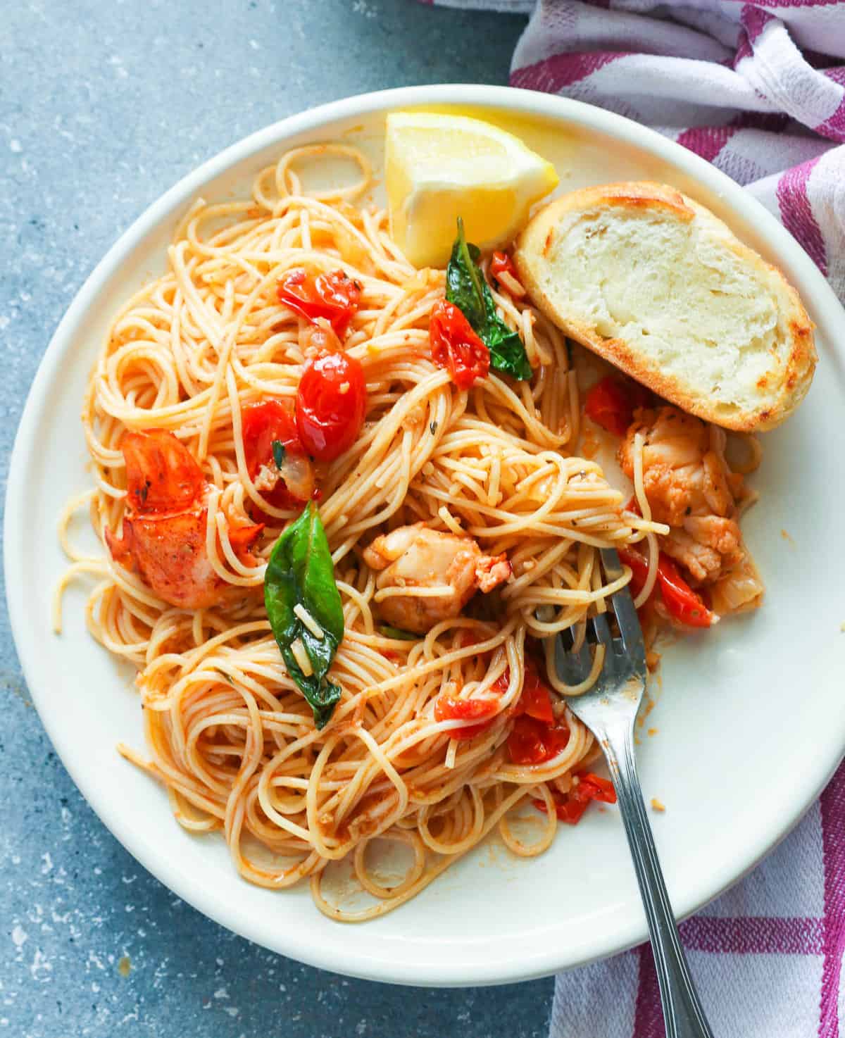 Insanely delicious lobster pasta on a white plate with homemade garlic bread