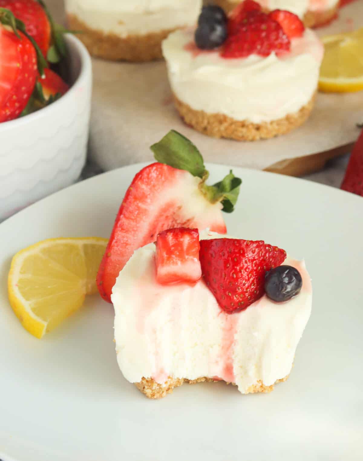 A bite is missing from a no-bake cheesecake bite topped with a strawberry and blueberry