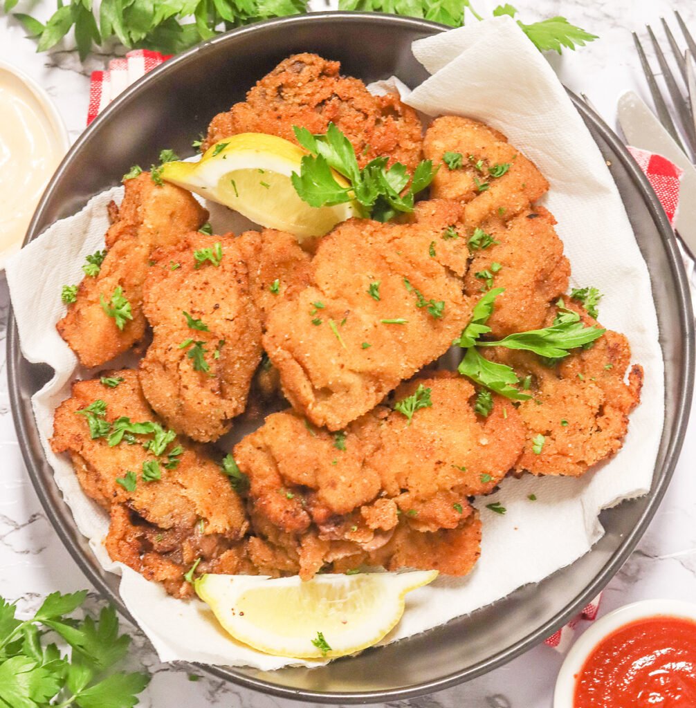 Crispy pan-fried chicken livers with lemon wedges on a white plate