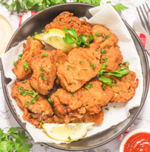 Crispy pan-fried chicken livers with lemon wedges on a white plate