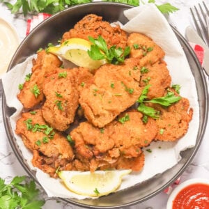 Crispy pan-fried chicken livers with lemon wedges on a white plate