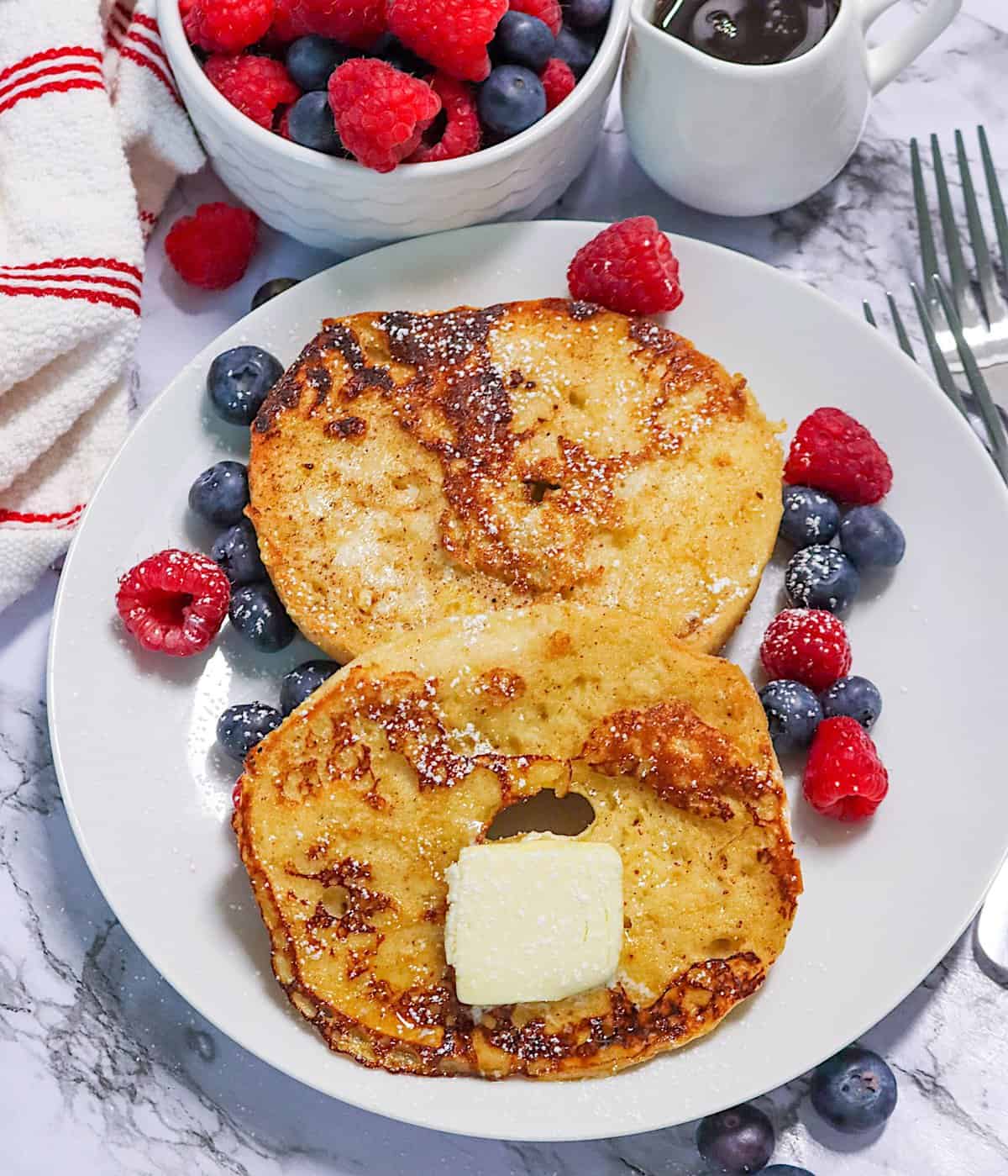 Melting a pat of butter on freshly made French Toast Bagels with berries