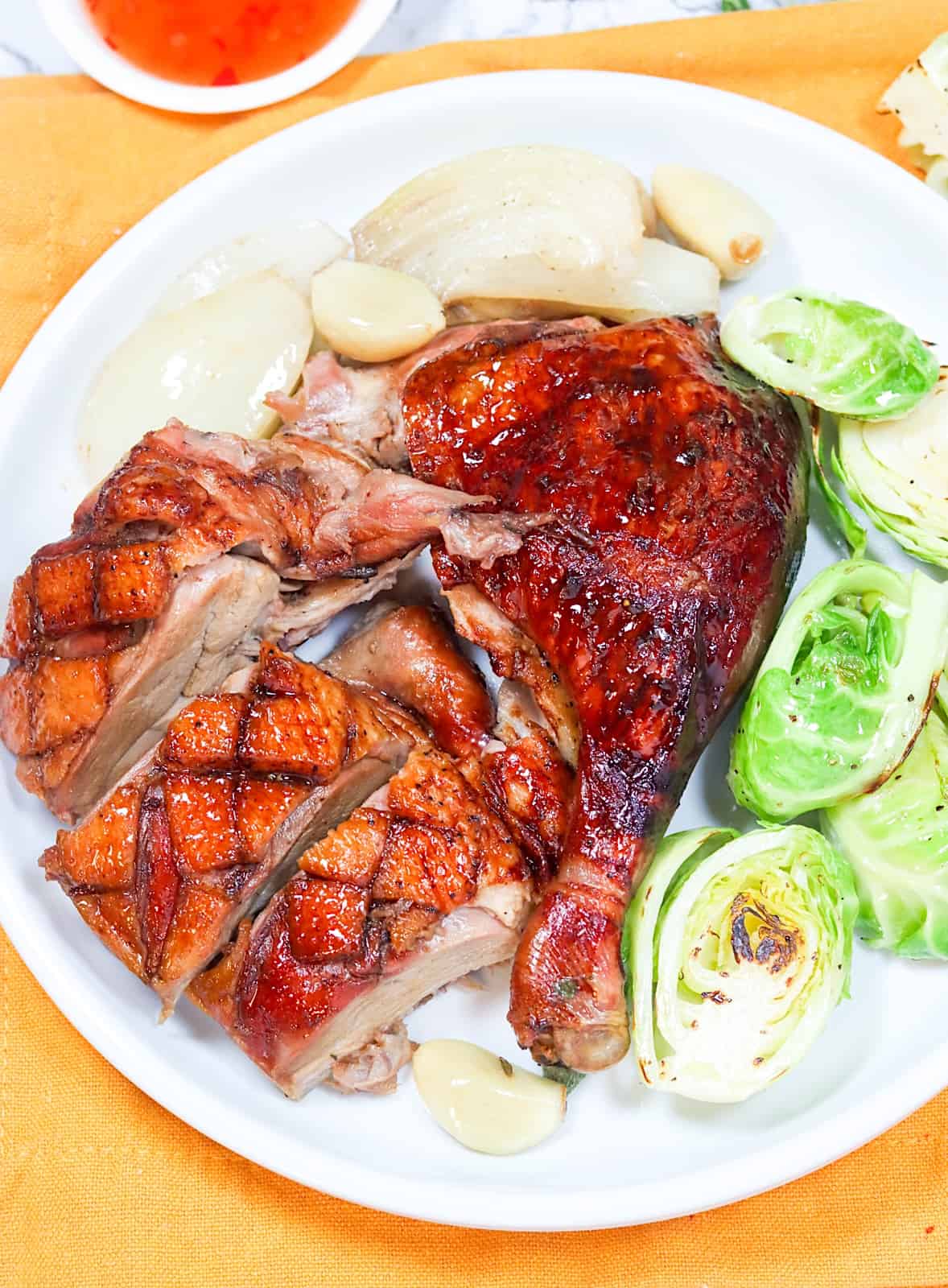 Serving Whole Roast Duck on a white plate with roasted Brussels sprouts for the perfect holiday dinner
