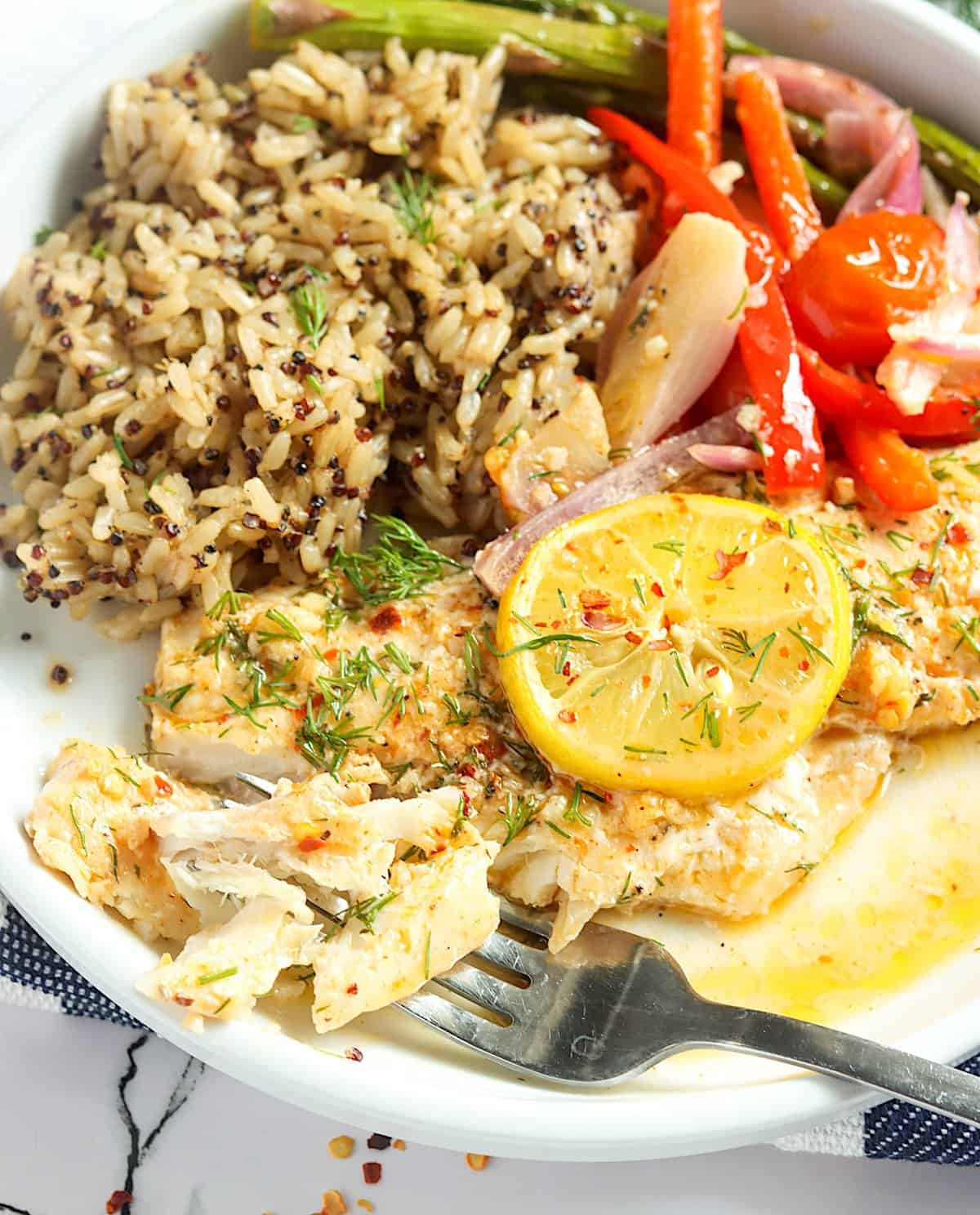 Baked Rockfish with seasoned rice, lemon slices, and delicious roasted vegetables for a complete meal
