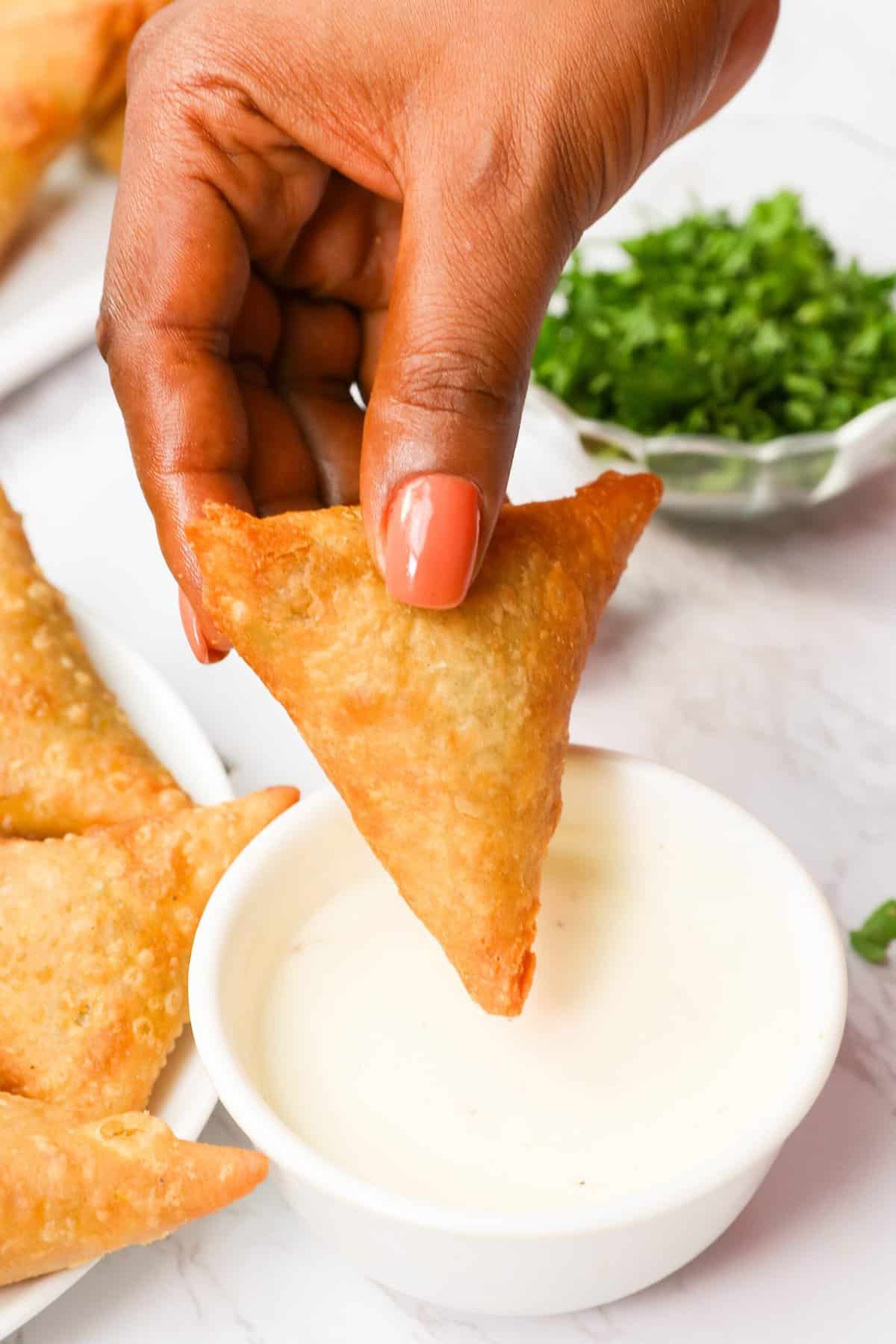 Dipping a steaming hot sambusa in a delectable dipping sauce