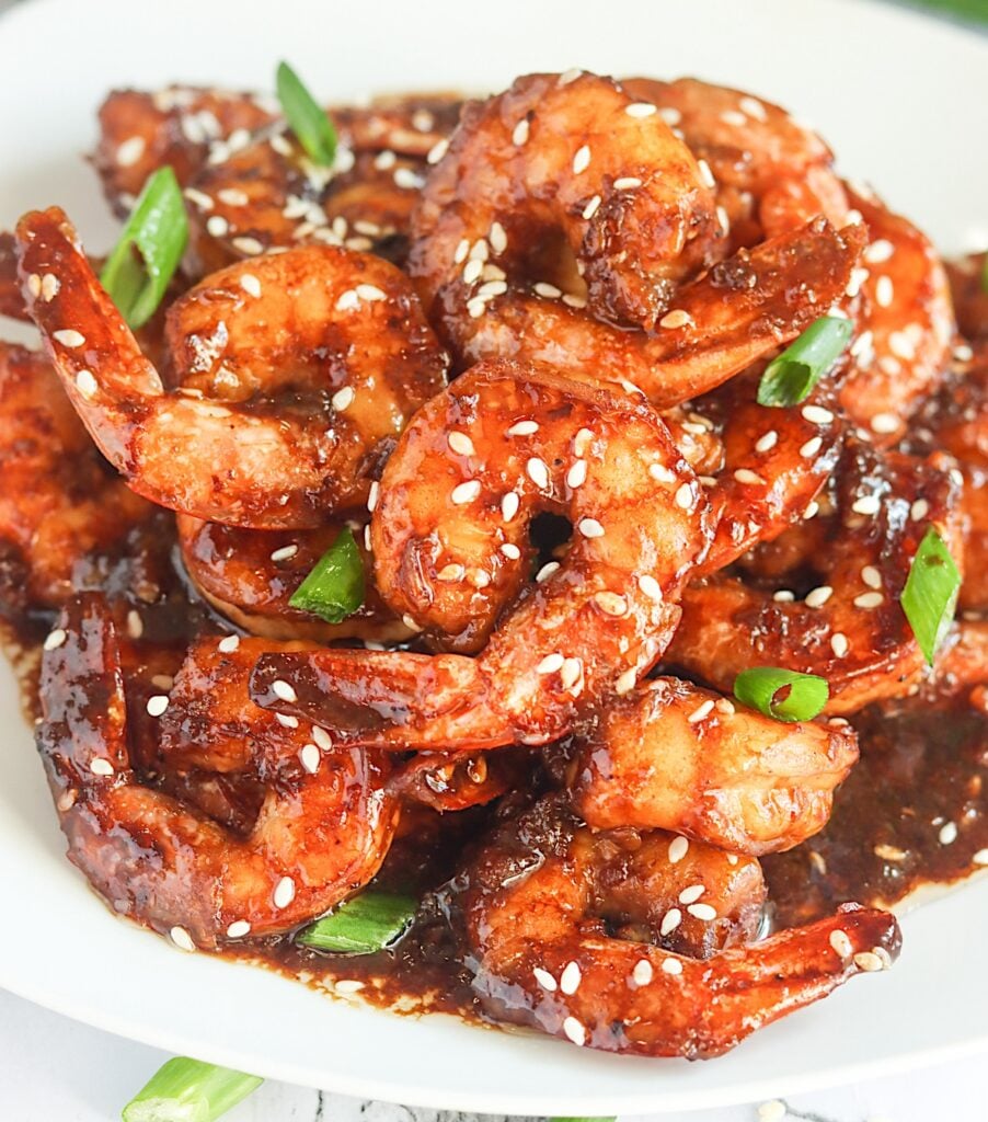 Enjoying steaming hot Teriyaki Shrimp garnished with sesame seeds and green onions on a white plate