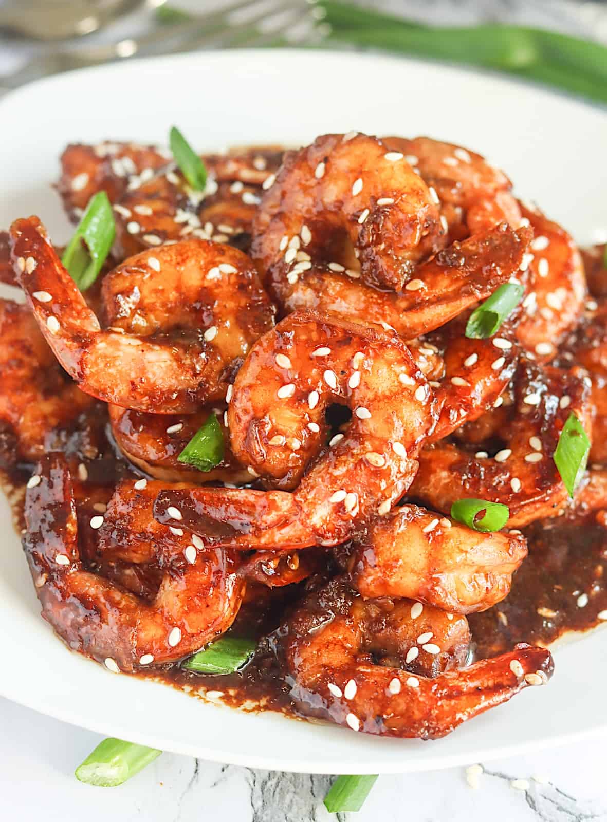 Enjoying steaming hot Teriyaki Shrimp garnished with sesame seeds and green onions on a white plate